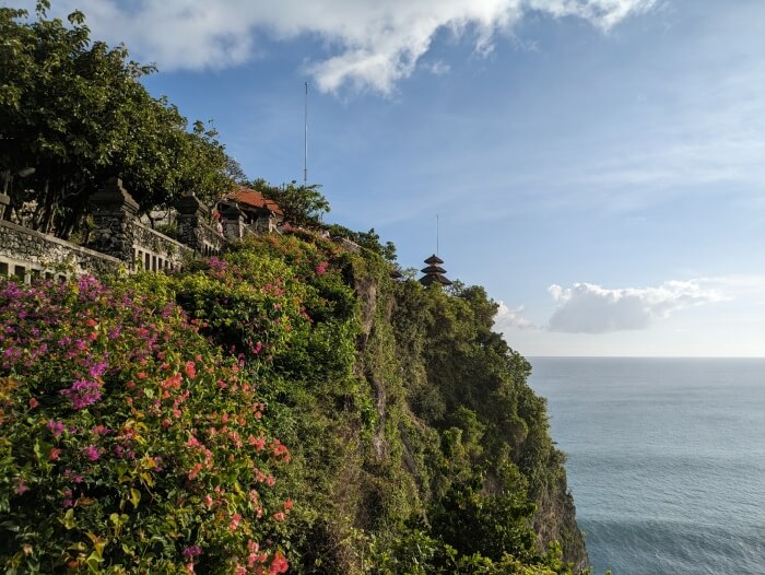 Acantilado lleno de vegetacion con el templo Uluwatu en lo alto y el mar abajo