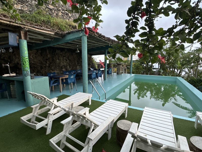 La zona de bar de nuestro alojamiento en Santo Antao, rodeada del verde paisaje, algunas hamacas y la piscina con agua de color verde