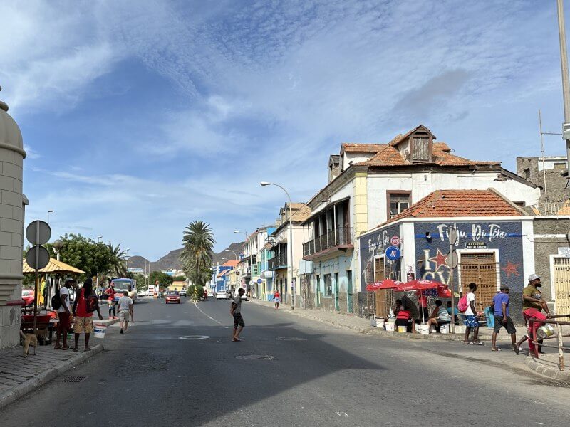 Varias personas locales paseando en su dia a dia por la colorida Avenida Libertadores de Africa, junto a la bahia de Mindelo