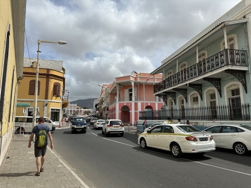 Casas coloniales de diferentes colores en una de las calles de Mindelo, donde tambien puede verse el trafico de coches