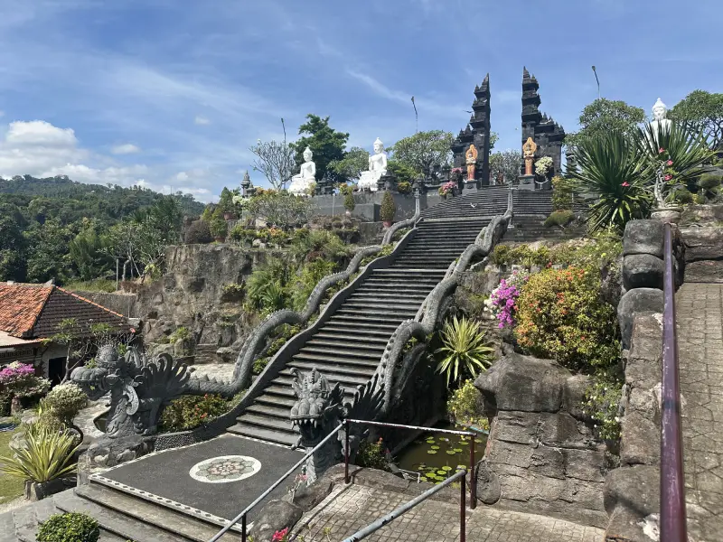 Escalinata de piedra que asciende hacia unas puertas tradicionales balinesas, rodeadas de relieves y esculturas de inspiración hindú y budista, en el templo Brahma Vihara Arama.