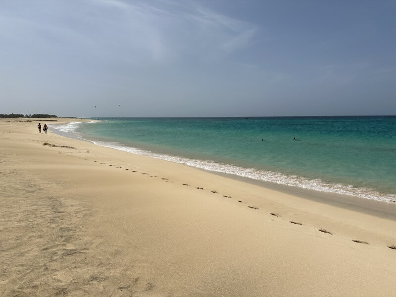 Vistas de la playa Ponta Preta donde pueden verse las aguas azul turquesa, la arena ligeramente dorada y dos personas andando hacia el horizonte