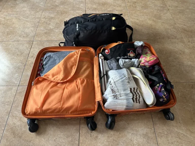 Maleta abierta llena con varias cosas que llevar en la maleta de viaje, como ropa, neceser, mochila, chanclas, etc.