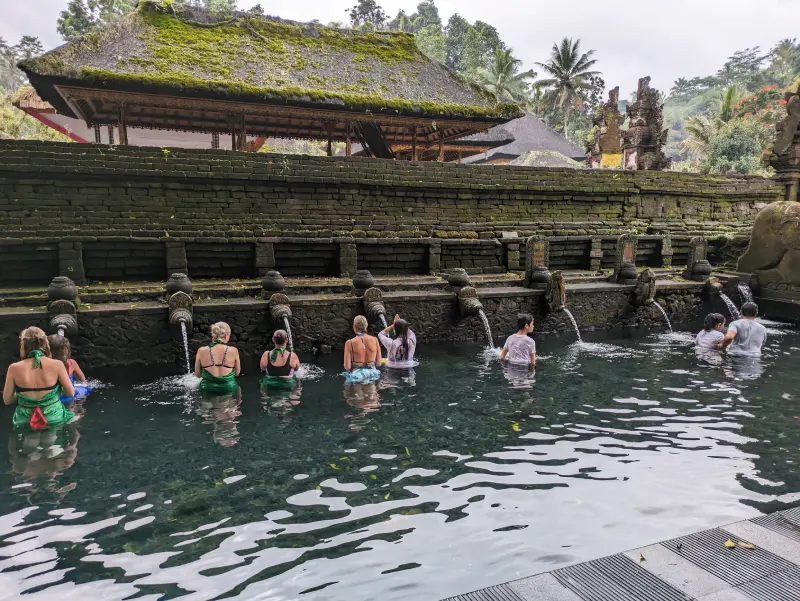 Ritual purificación Tirta Empul Varias personas frente a las fuentes de la piscina del templo Tirta Empul de Bali, realizando el ritual de purificación