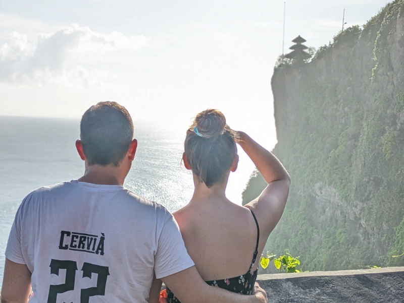 Vistas Pura Luhur Uluwatu Jordi y yo de espaldas mirando el acantilado sobre el mar lleno de vegetacion con el templo Uluwatu en lo alto