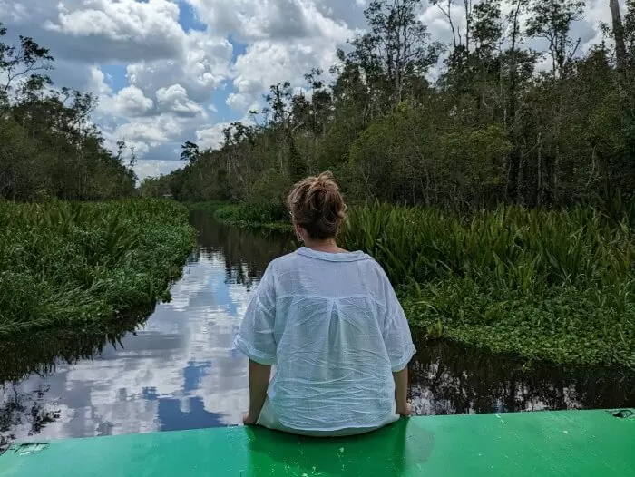 Yo sentada en nuestro klotok de la excursion para ver orangutanes en Borneo contemplando las vistas del rio y la selva de Tanjun Puting